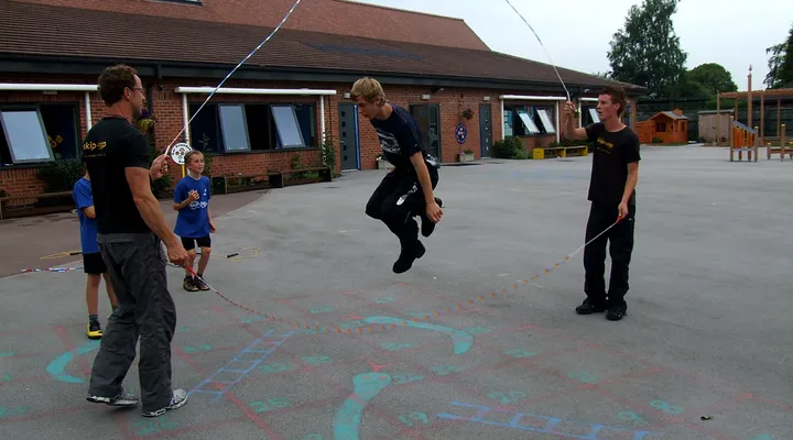 Pupils jump a long rope turned by skip-hop coaches in a school playground