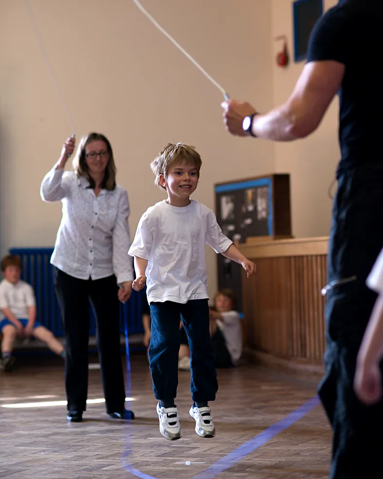 A teacher and a pupil jump a long rope together while a coach turns