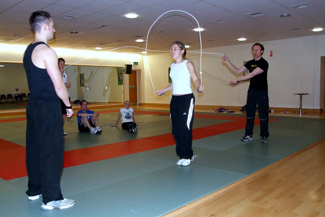 A teacher jumps a long rope turned by a skip-hop coach at a staff skipping training day