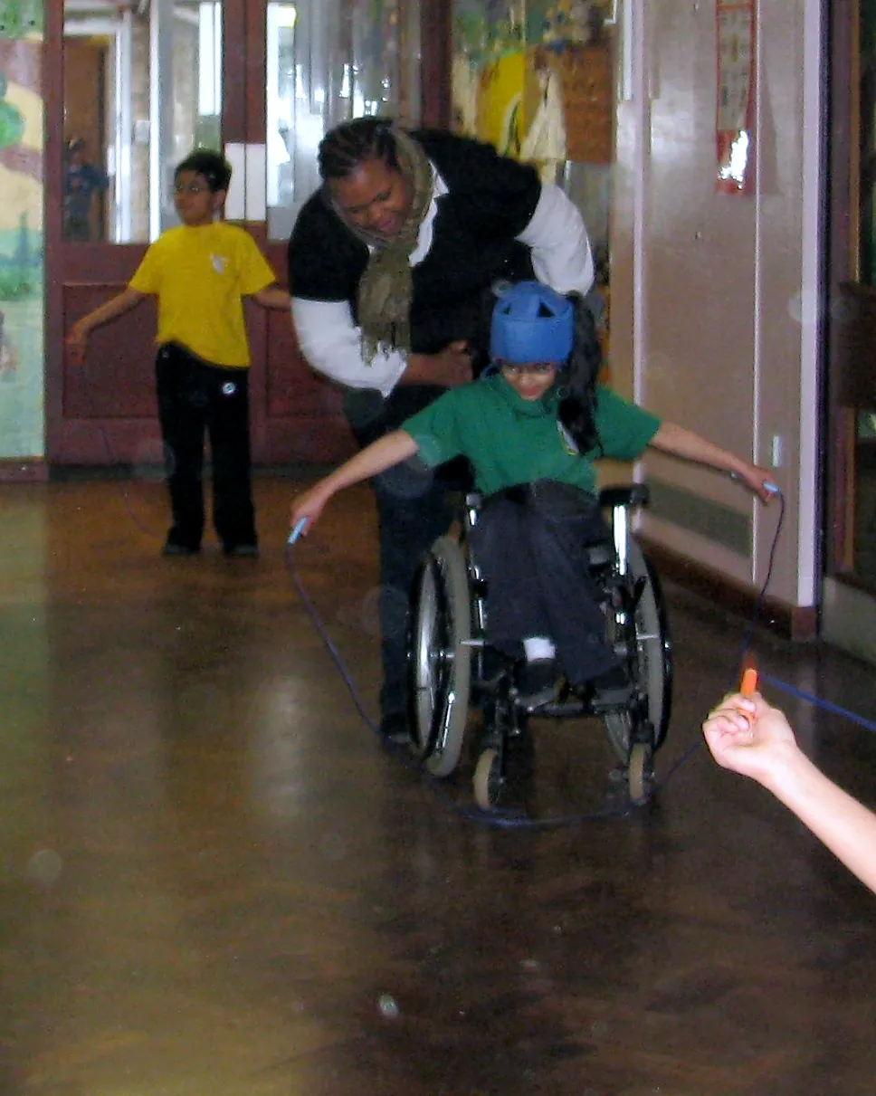 A pupil using a wheelchair joins in an adapted skipping activity with an adult supporting