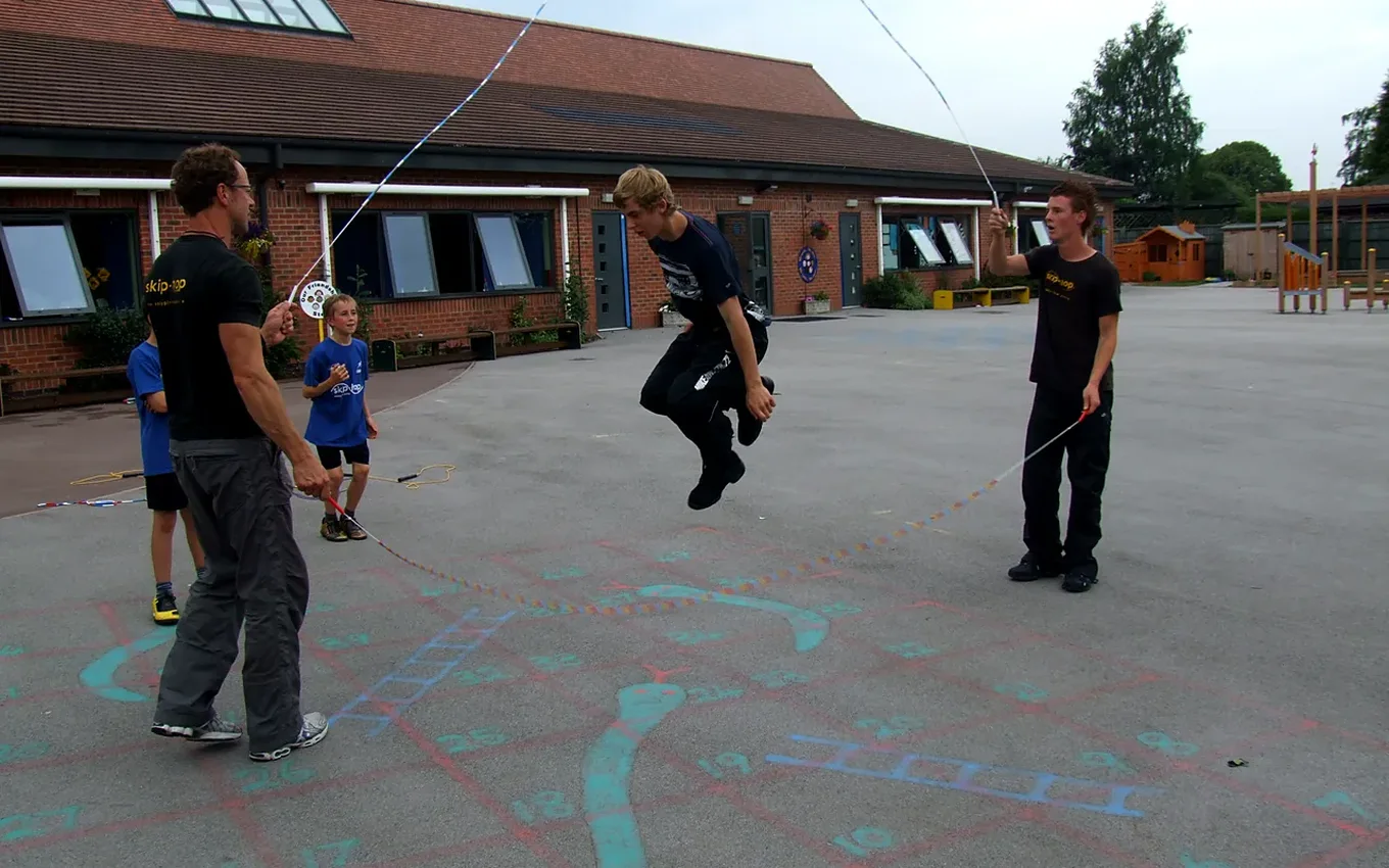 Pupils jump a long rope turned by skip-hop coaches in a school playground