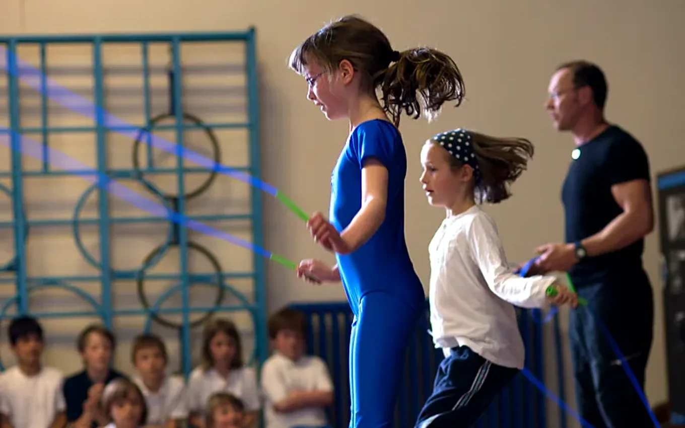 Two pupils skip side by side in a PE lesson while a skip-hop coach helps